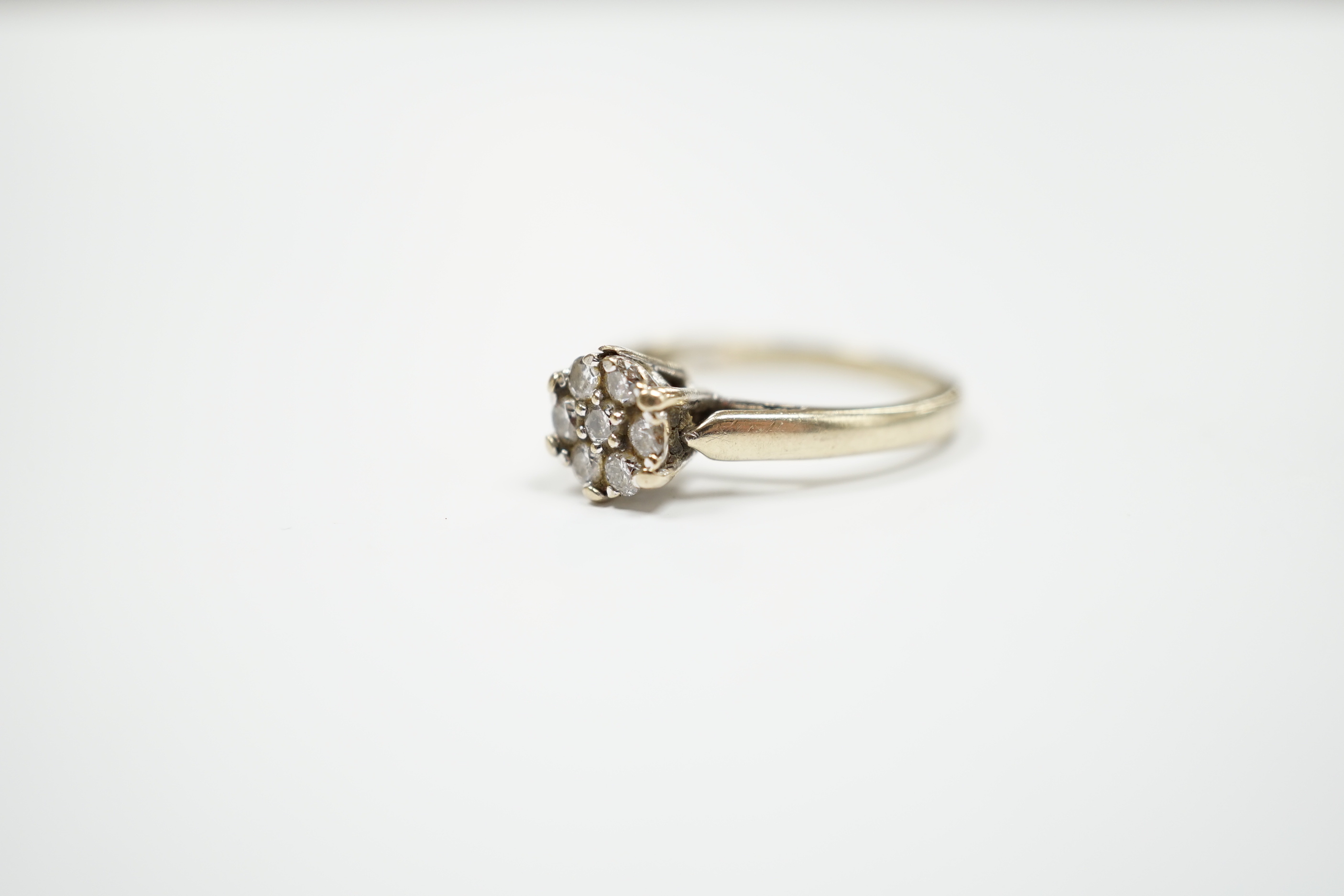 A 750 white metal and seven stone diamond set circular cluster ring, size M, gross weight 3.2 grams.